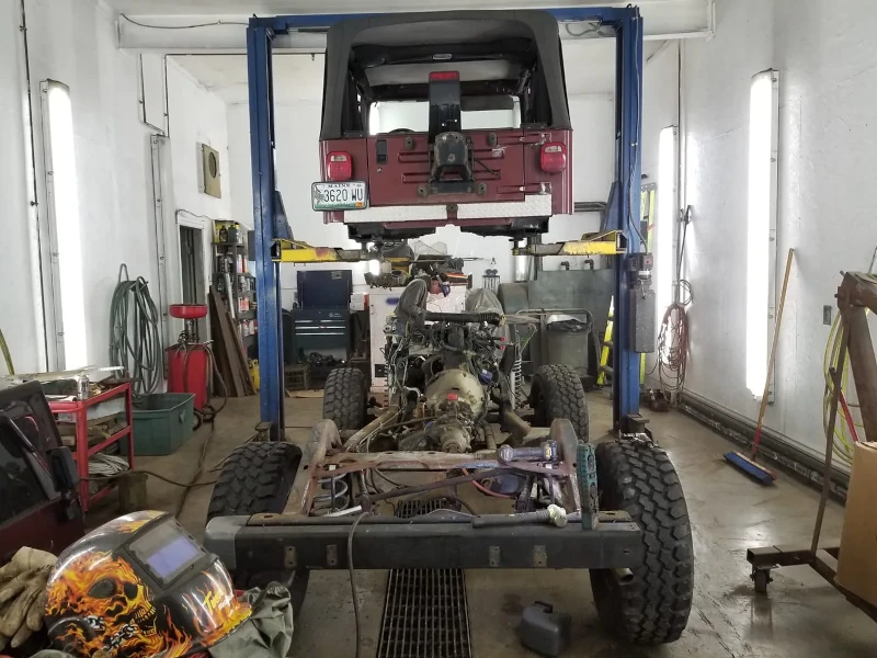 Jeep Wrangler body suspended in the air on a lift, with the frame and motor below